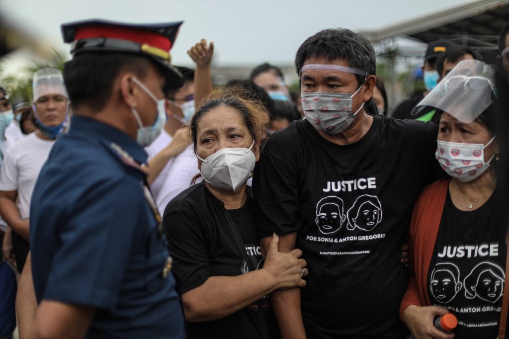 A police officer speaks with family members of the Gregorios during the funeral march for mother and son Sonia and Frank Anthony Gregorio in the town of Paniqui in Tarlac province on Dec. 27. (Photo by Jire Carreon)