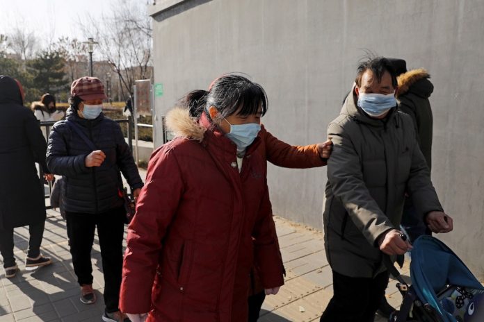 People wearing face masks walk along a street, following reports of new COVID-19 cases in Beijing, China on Jan. 11. (Photo by Tingshu Wang/Reuters)