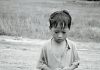A black and white photo of a poor boy in rural Asia.