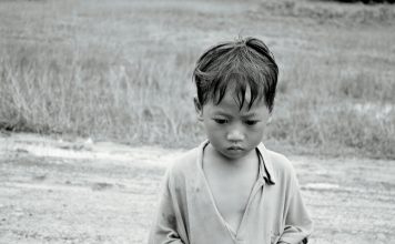 A black and white photo of a poor boy in rural Asia.